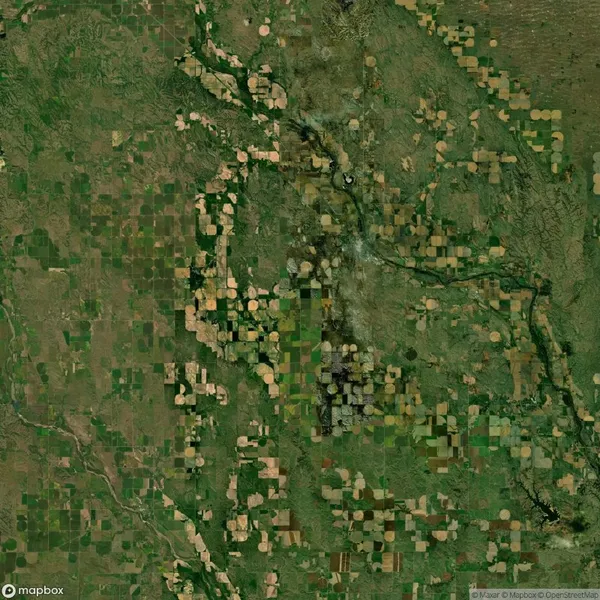 A satellite view of a rural landscape showing an array of irregularly shaped green and brown agricultural fields, intersected by rivers and roads.