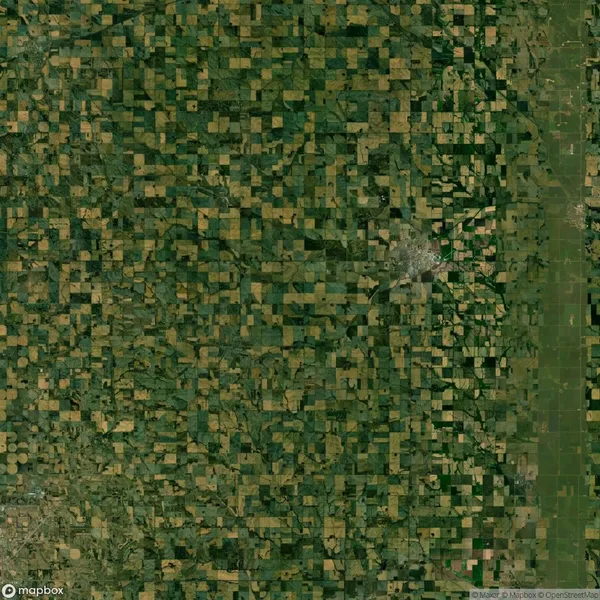 Aerial view of a vast, patchwork landscape with rectangular farmland plots and a small urban area on the right.