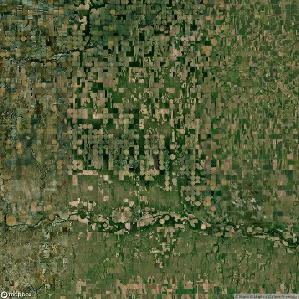 Aerial view of agricultural fields with rectangular and circular patterns, interspersed with patches of greenery and a river running through the lower part of the image.
