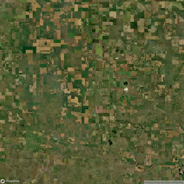 Aerial view of a patchwork landscape featuring farmland fields of varying shades of green and brown, arranged in rectangular plots.