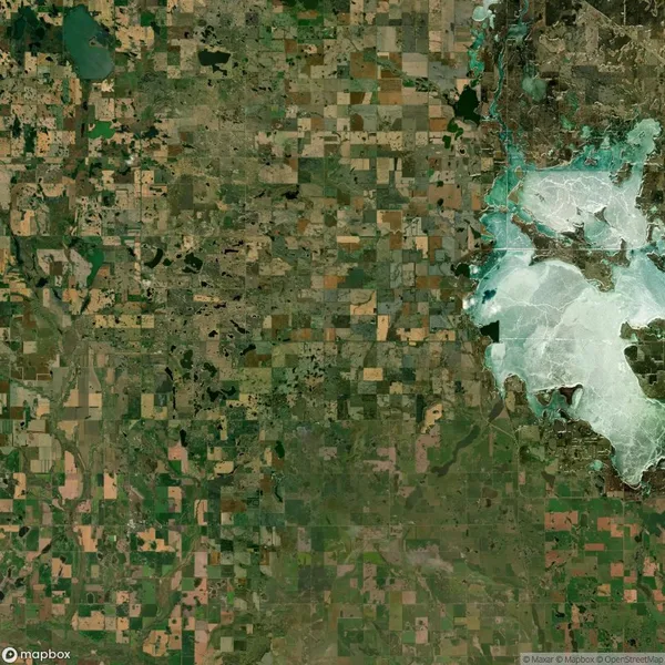 Satellite image of a landscape with a patchwork of agricultural fields on the left and a large white area, likely a body of water or salt flat, on the right.