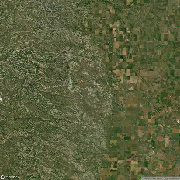 Satellite image showing a contrast between rugged terrain on the left and a patchwork of agricultural fields on the right.