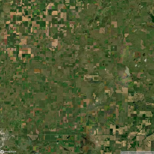 Aerial view of a patchwork landscape with fields in varying shades of green and brown, intersected by roads, in a rural area.