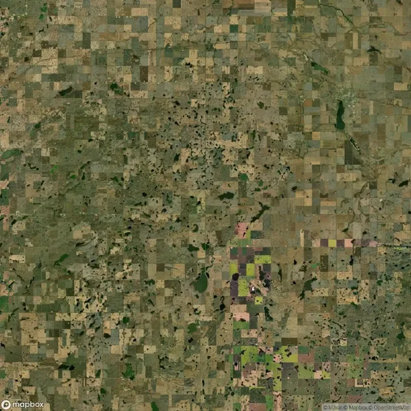 Aerial view of a patchwork quilt pattern of agricultural fields with varying shades of green and brown, interspersed with small water bodies and patches of vegetation.