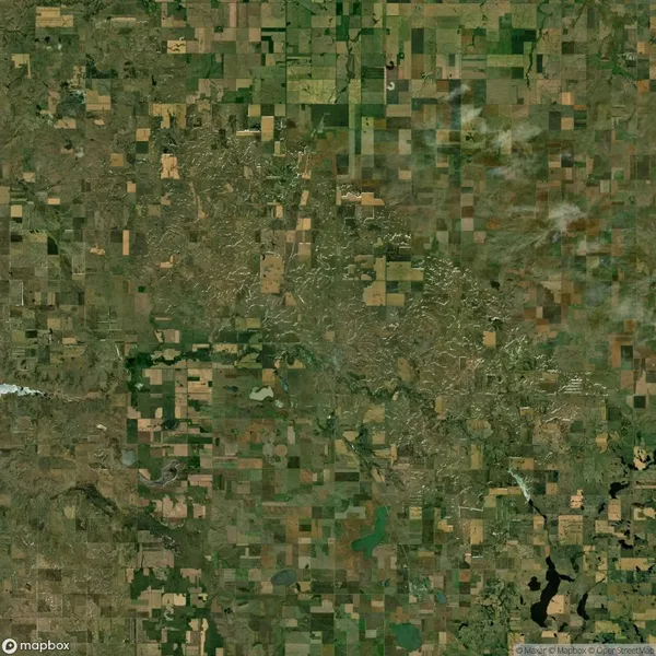 Aerial view of a rural landscape showcasing a patchwork of agricultural fields in various shades of green and brown, intersected by irregular patterns of vegetation.