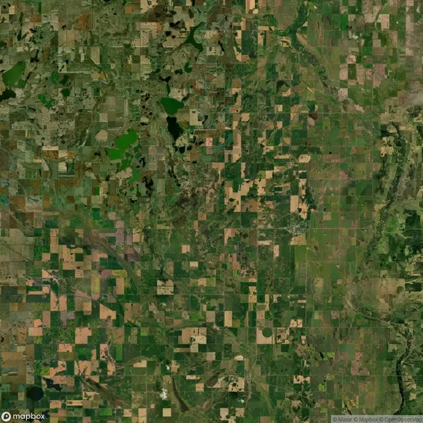 Aerial view of a patchwork landscape, showing a mosaic of agricultural fields in varying shades of green and brown, intersected by roads and natural water features.