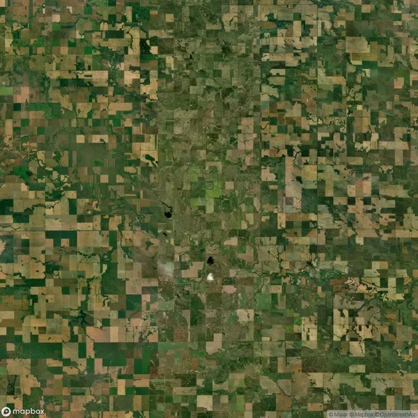 Aerial view of a patchwork landscape featuring rectangular agricultural fields in various shades of green and brown, divided by roads and sparse vegetation.