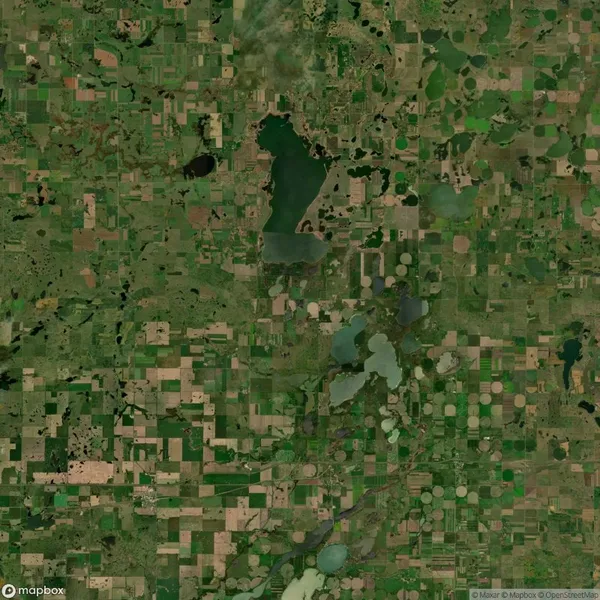 Aerial view of a rural landscape with a patchwork of green and brown fields, several lakes, and circular crop patterns.