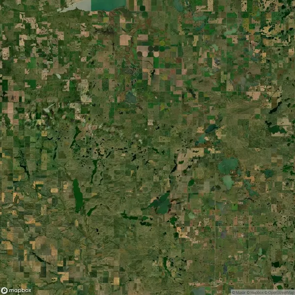 Aerial view of a large patchwork of agricultural fields and green land, interspersed with a few lakes and roads, under a partly cloudy sky.