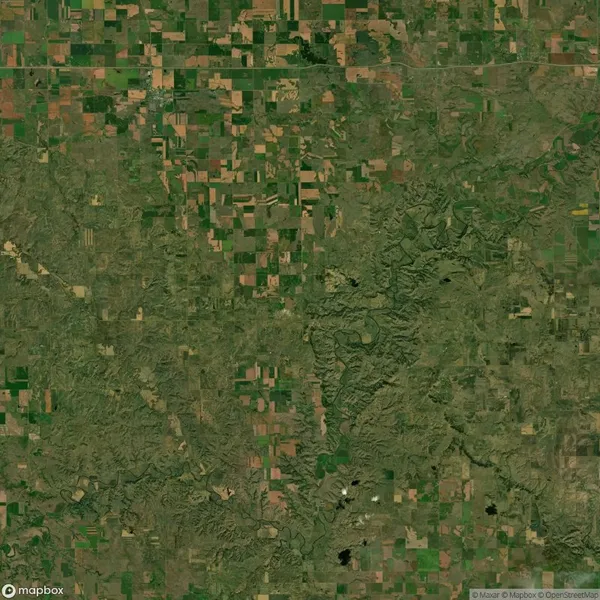 Aerial view of a vast landscape featuring a patchwork of agricultural fields and green vegetation, crossed by jagged, winding lines suggesting natural features or erosion patterns.