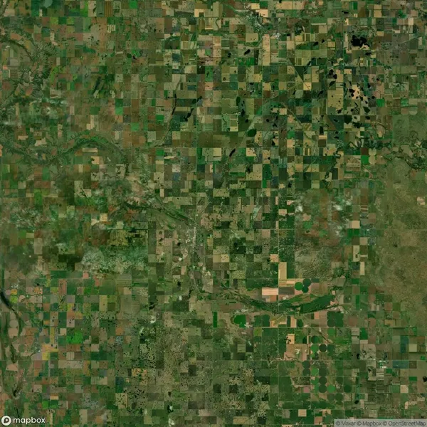 Satellite view of a rural landscape featuring a patchwork of agricultural fields and intersecting roads, with a river meandering through the center.