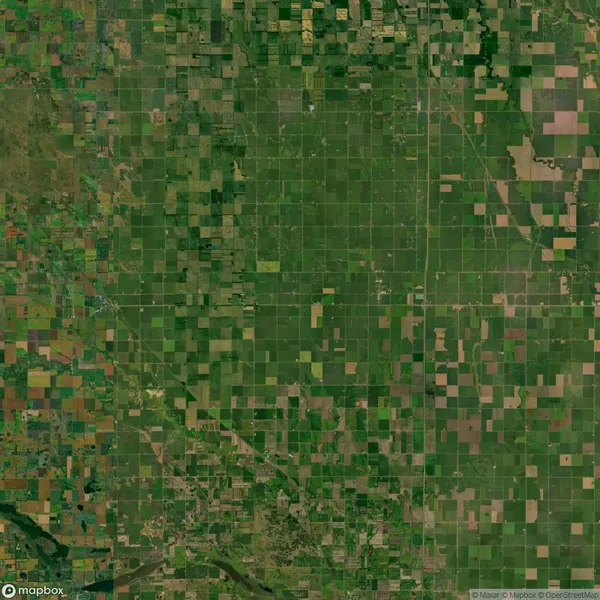 Aerial view of a patchwork pattern of agricultural fields, with varying shades of green and brown across a flat landscape. Roads and waterways intersect some areas.