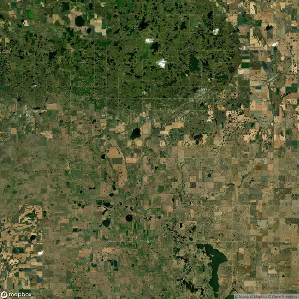 A satellite view showing a patchwork of agricultural fields and scattered bodies of water, interspersed with green forested areas and sparse urban development.