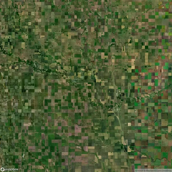 Aerial view of a patchwork quilt-like landscape with numerous rectangular agricultural fields in varying shades of green and brown. A river meanders through the center.