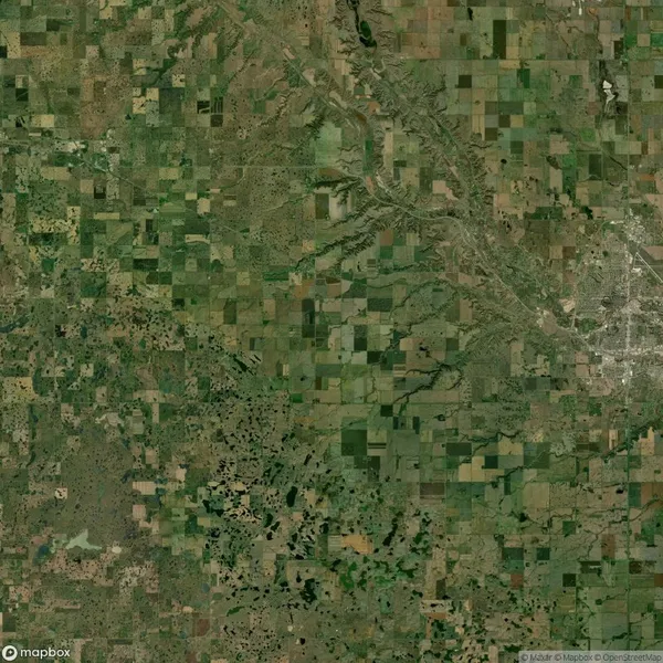 Aerial view of a patchwork of agricultural fields and rural landscape with roads and sparse vegetation, showing a mixture of green and brown tones.