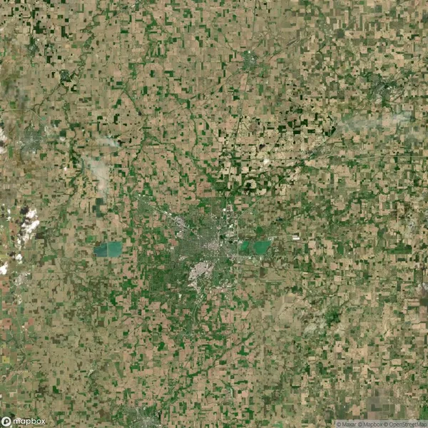 Satellite view of a landscape featuring a central urban area surrounded by a patchwork of agricultural fields, displaying patterns of green and brown.
