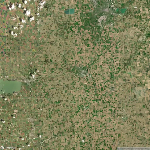 Satellite image of a vast agricultural landscape with patchwork fields, scattered clouds, and small urban areas near the top edge.