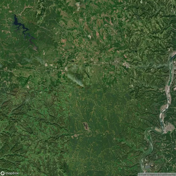 Aerial view of a dense green landscape with a visible smoke plume in the center and a river winding through the right side.