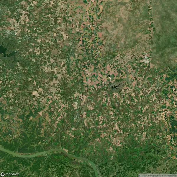 Satellite view showing a patchwork of agricultural fields, green vegetation, and a winding river at the bottom.
