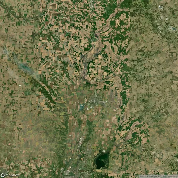 Satellite view of a rural landscape with fields, patches of green, a town, and a visible lake near the bottom.