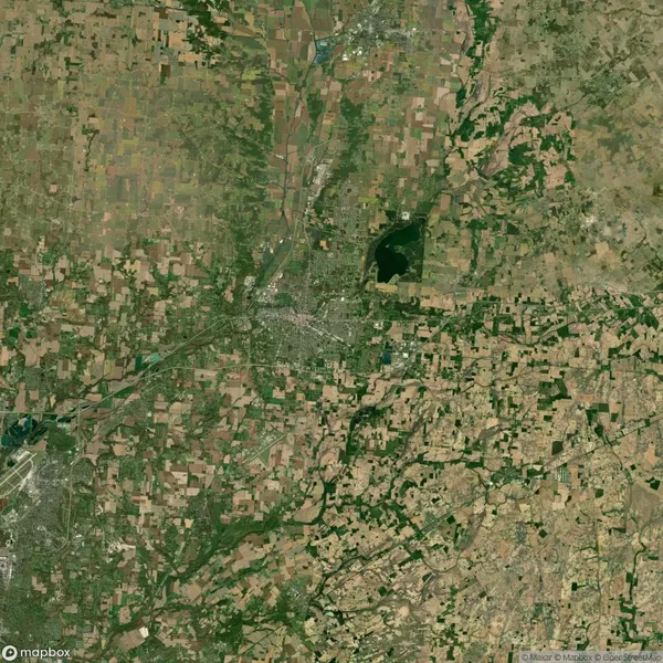 Aerial view of a landscape with a city center surrounded by a patchwork of fields and a large body of water to the northeast.
