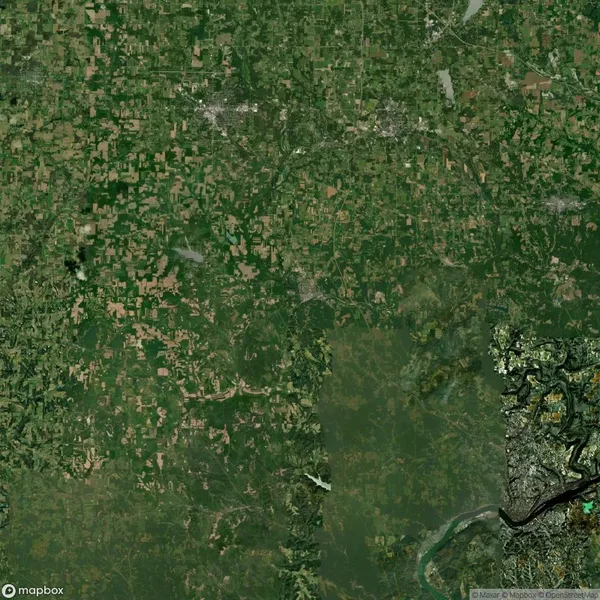 Aerial view of a landscape featuring a patchwork of green fields, forests, and urban areas. A river meanders through the lower right corner.