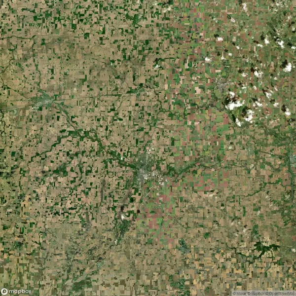 Aerial view of a rural landscape with patchwork fields, roads, and a scattered settlement in the center. Mostly brown and green tones.