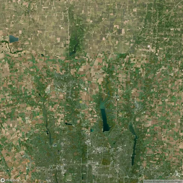 Aerial view of a landscape with a mix of agricultural fields, patches of forest, and bodies of water. Roads and structures are visible throughout the area.