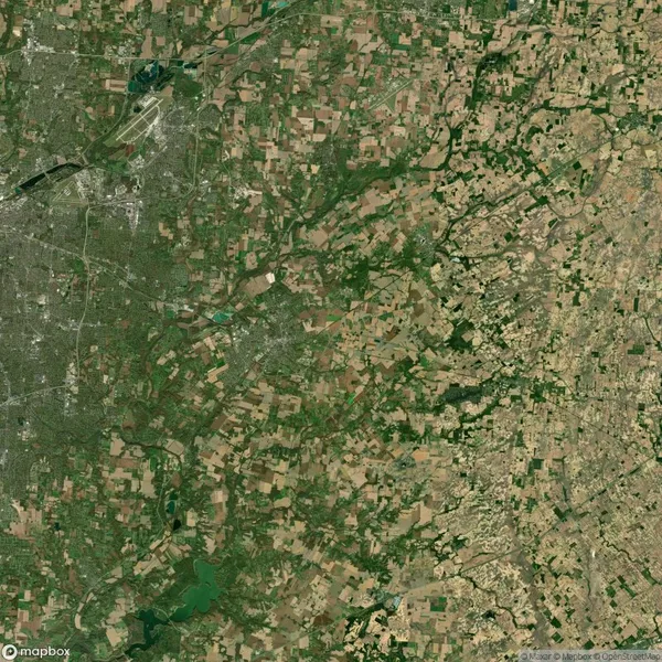 Aerial view of a rural landscape with a mix of fields, forests, and towns. Roads and waterways are visible. Areas of dense green vegetation contrast with brown, open patches of land.