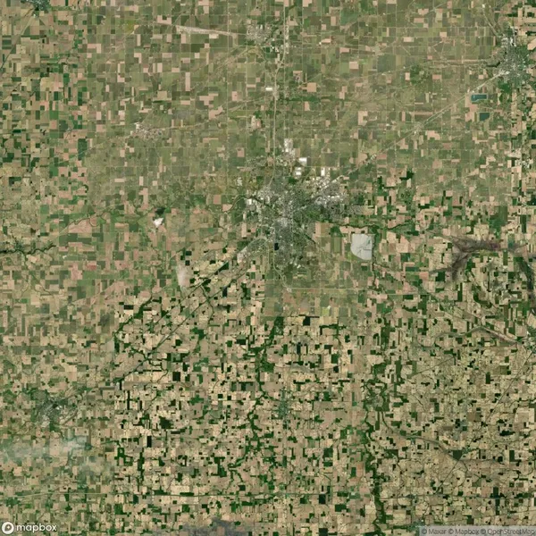 Satellite view of an expansive patchwork landscape with fields surrounding a central urban area, characterized by a grid-like pattern of roads and agricultural plots.