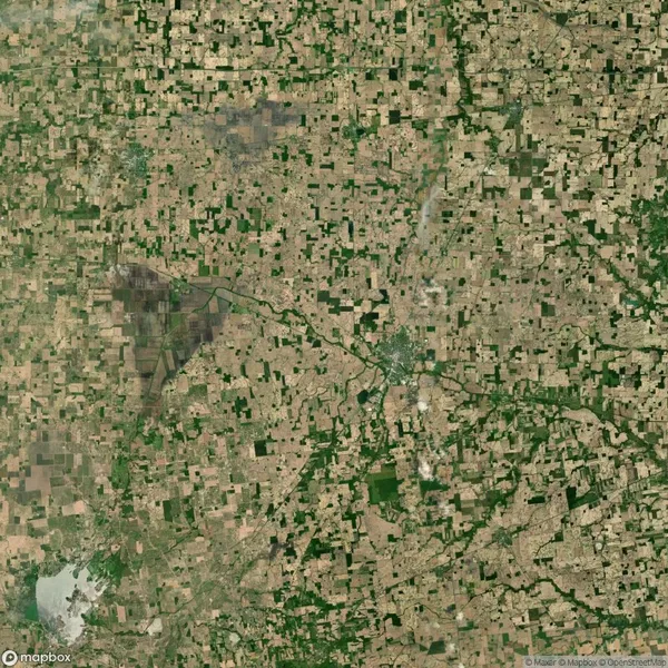 Aerial view of a vast patchwork of agricultural fields interspersed with small green areas. A road cuts diagonally through the landscape.