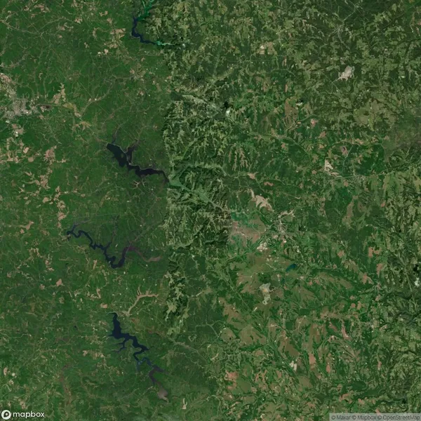 Aerial view of a landscape divided by a river with forests on one side and fields on the other, featuring multiple water bodies and varying terrain.