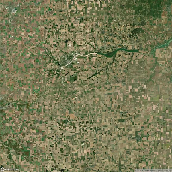 Aerial view of a sprawling patchwork of agricultural fields with a meandering river and a small urban area in the center. Sparse vegetation can be seen in patches.