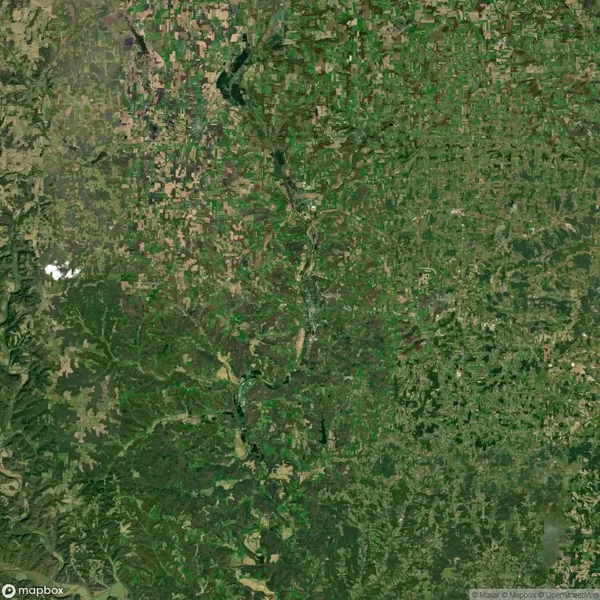Aerial view of a landscape with patches of green vegetation and brown areas, indicating agricultural fields and natural terrain; a river meanders through the center of the image.