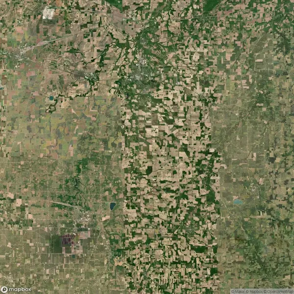 Aerial view of a large patchwork of farmland with various shades of green and brown, interspersed with small wooded areas and waterways.