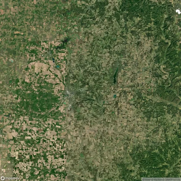 Aerial view of a rural landscape with a mix of green and brown patches, indicating areas of vegetation and farmland, intersected by roads.
