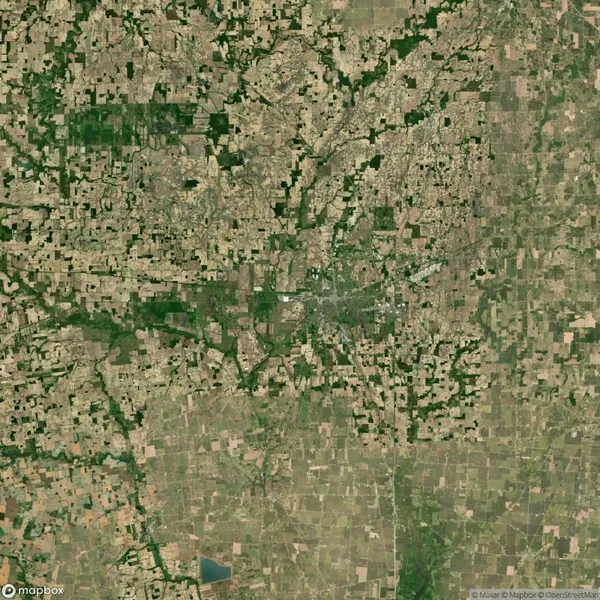 Aerial view of a patchwork landscape featuring agricultural fields and scattered green areas with a small urban settlement at the center.