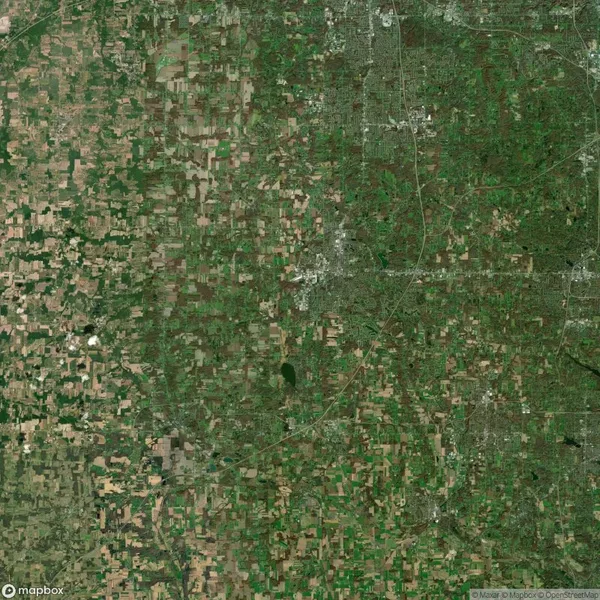 Satellite view of a landscape featuring a patchwork of agricultural fields, a scattering of small bodies of water, and an urban area with visible roads and infrastructure.