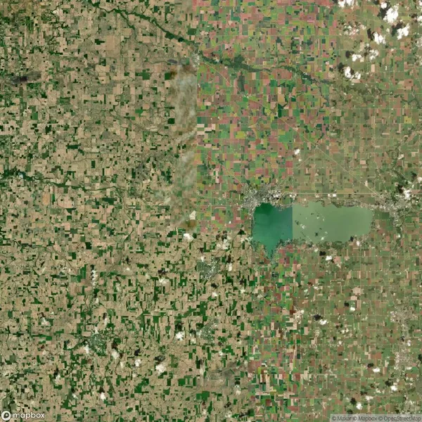 Aerial view of a patchwork landscape featuring farmland and a central lake, with scattered clouds in the sky.
