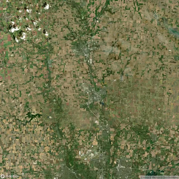 Aerial view of a rural landscape with patchwork farmland, scattered clouds in the top left, and a winding road cutting through the center.