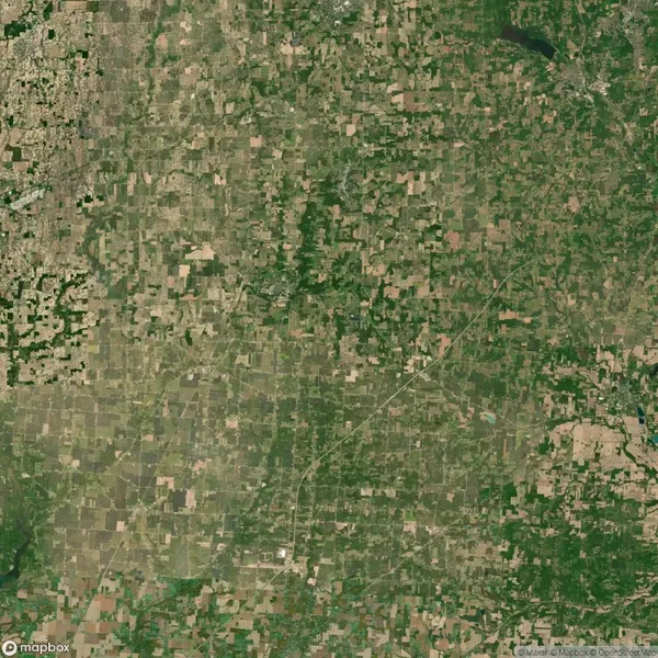 Aerial view of a patchwork landscape with various shades of green and brown, indicative of farmland and natural vegetation, intersected by roads and small clusters of development.