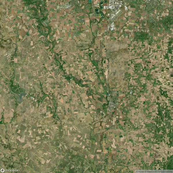 Aerial view of a rural landscape with patchwork fields, winding rivers, and clusters of buildings in the upper right corner.