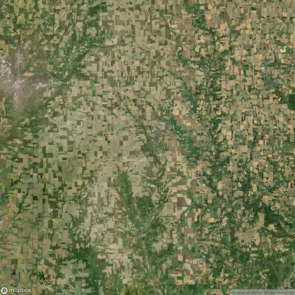 Aerial view of a vast farmland landscape with a patchwork of green and brown fields, interspersed with small wooded areas and a winding river.