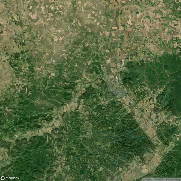 Aerial view of a landscape showing forests, fields, and a small settlement. Roads and patches of greenery and farmland are visible.