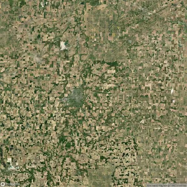 Satellite view of a large, irregular patchwork of agricultural fields, interspersed with small green areas, depicting rural landscape patterns.