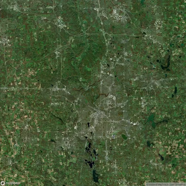 Satellite view of a densely populated urban area surrounded by green rural land and bodies of water, crisscrossed by roads and highways.