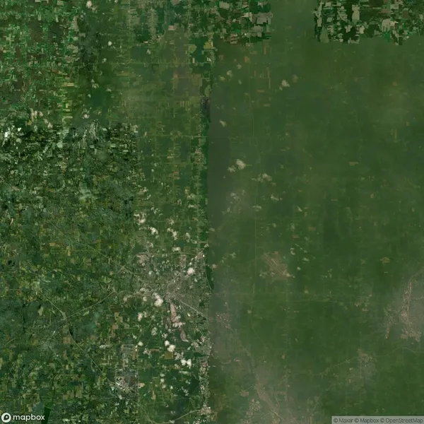 Aerial view of a landscape showing a stark contrast between urban and rural areas, with dense greenery on the right and developed land with visible roads and buildings on the left.