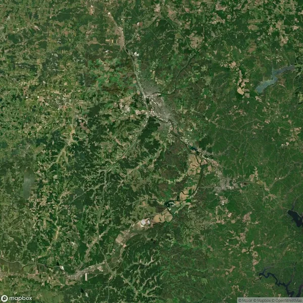 Aerial view of a landscape with sprawling greenery and a winding river, featuring scattered patches of urban development and a few small bodies of water.