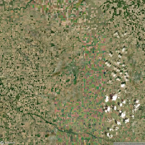 Aerial view of a patchwork landscape with rectangular agricultural fields, scattered clouds, and dispersed greenery.