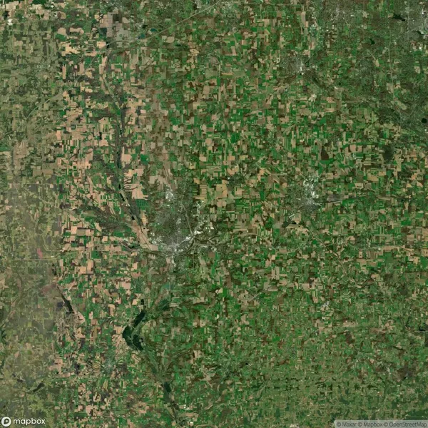 Aerial view of a patchwork landscape with fields, small forests, and urban areas snaking through the image, indicative of a rural region with agricultural and residential zones.